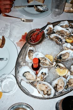 A platter of fresh oysters on ice with lemon wedges and hot sauce, perfect for seafood lovers.
