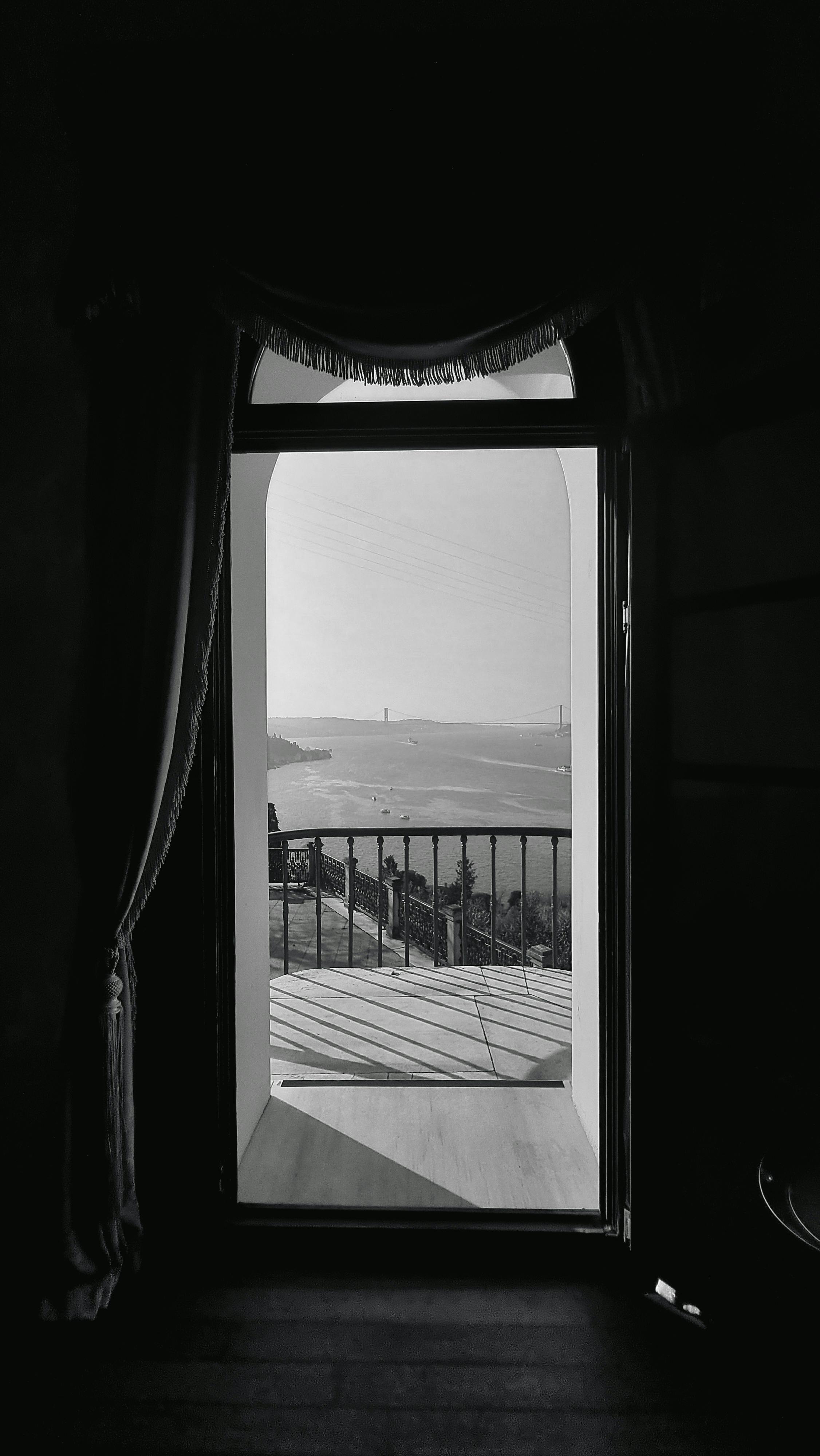 A black and white view through a doorway overlooking water and a distant bridge.