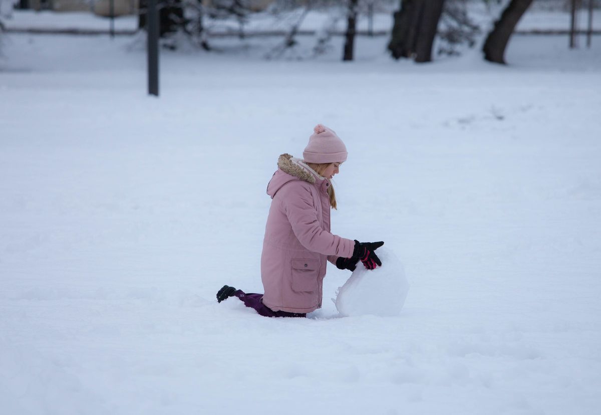Child building a snowman in a winter park