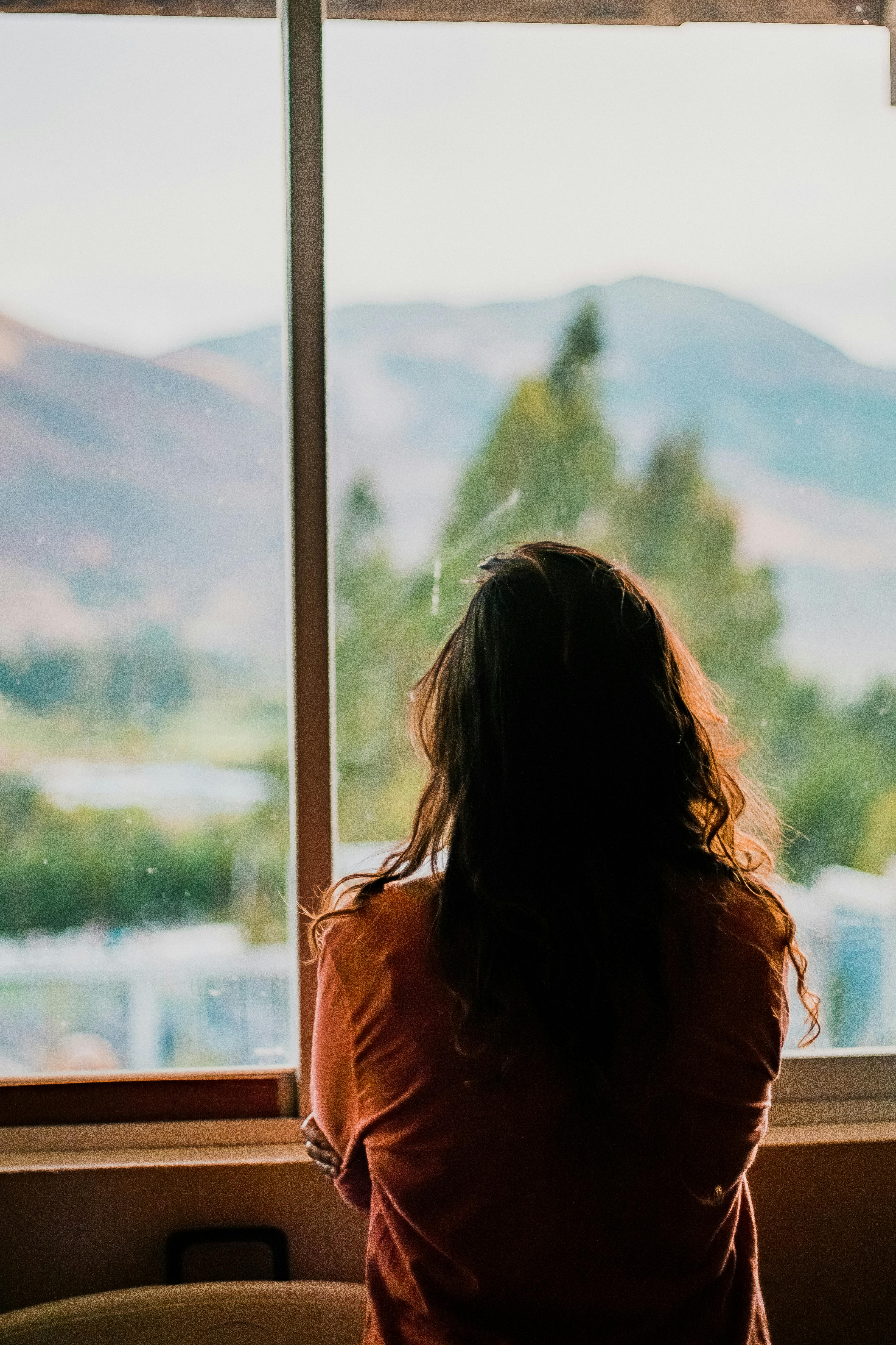 A woman looking out the window inside her room. | Photo: Pexels