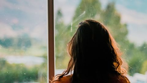 Silhouette of a woman looking out a window at a scenic mountain view in Cajamarca, Peru.