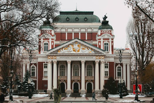Snowy winter scene of Ivan Vazov National Theatre in Sofia, showcasing Baroque architecture.