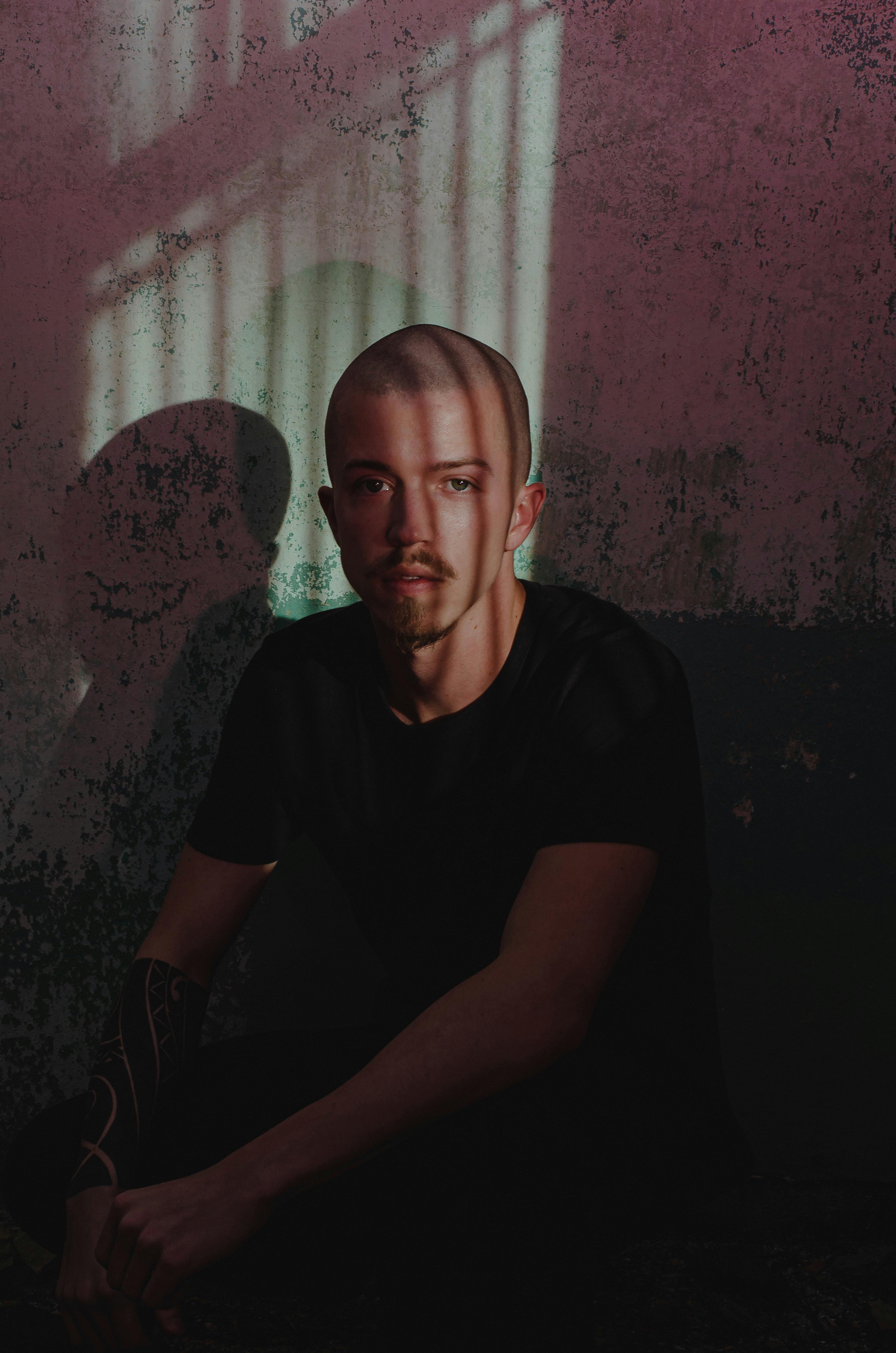 Dramatic portrait of a man with shadow patterns on a textured wall, evoking a mysterious mood.