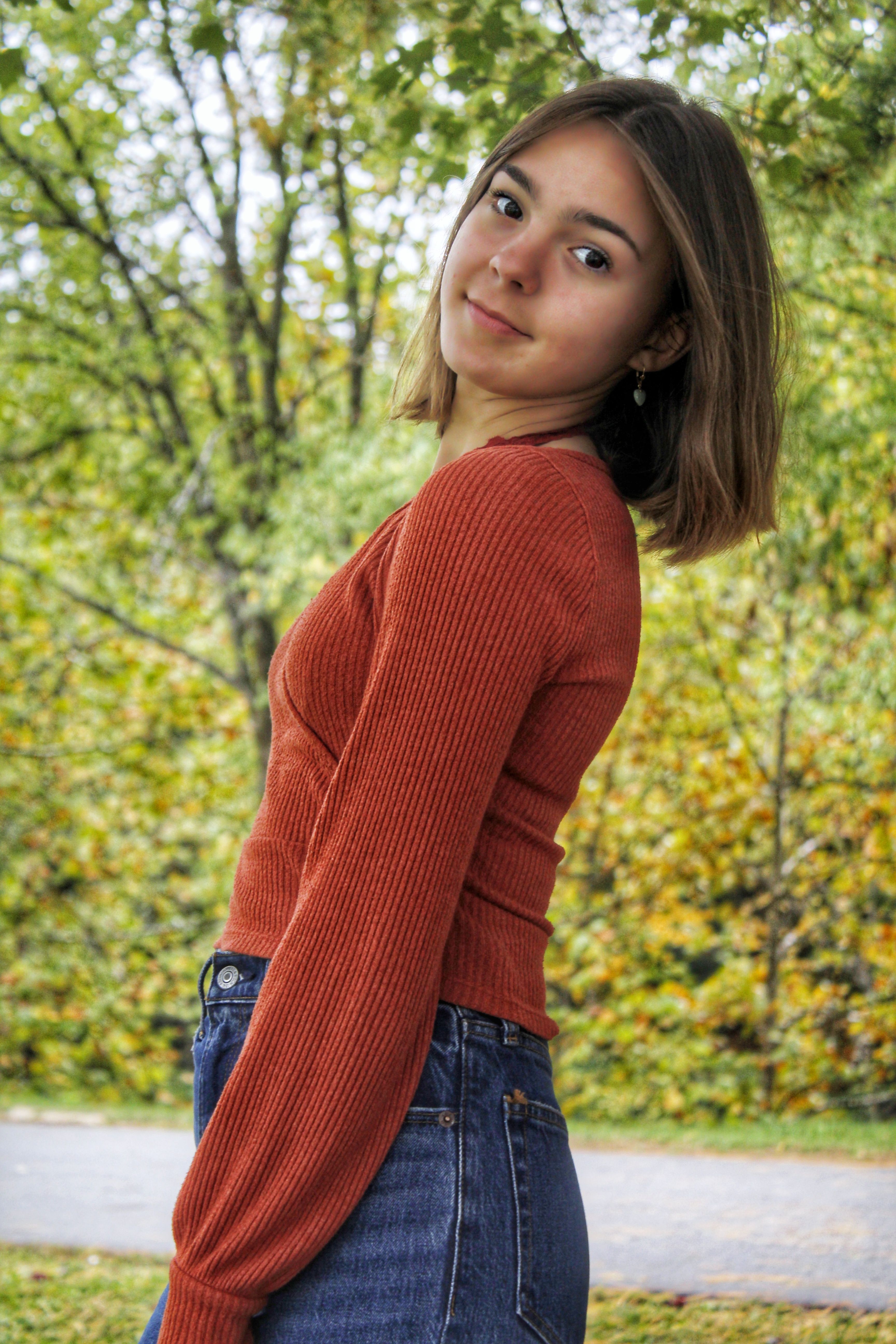 Young woman in orange sweater posing outdoors in autumn.