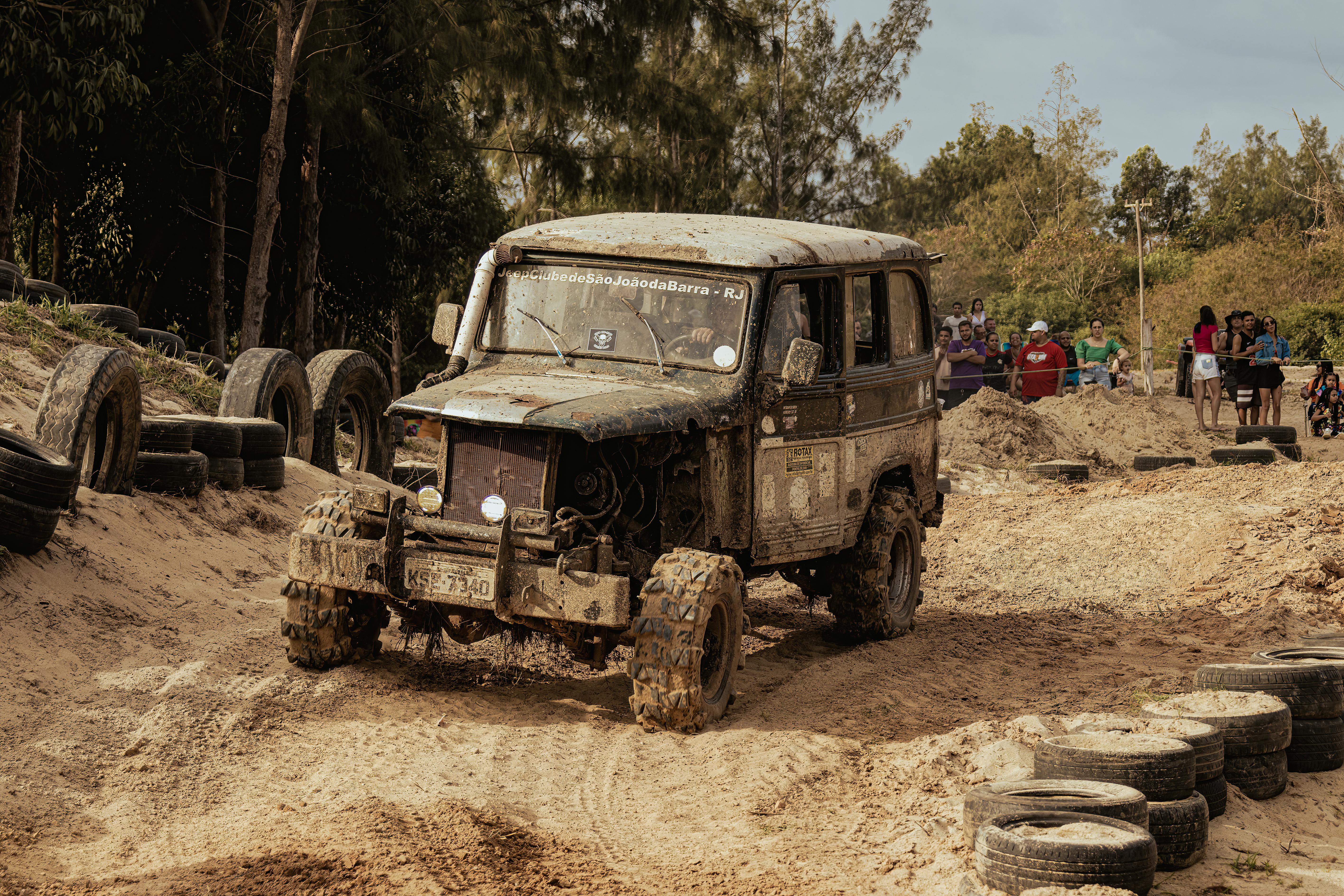 An off-road jeep navigating through a rough and muddy track with spectators watching.