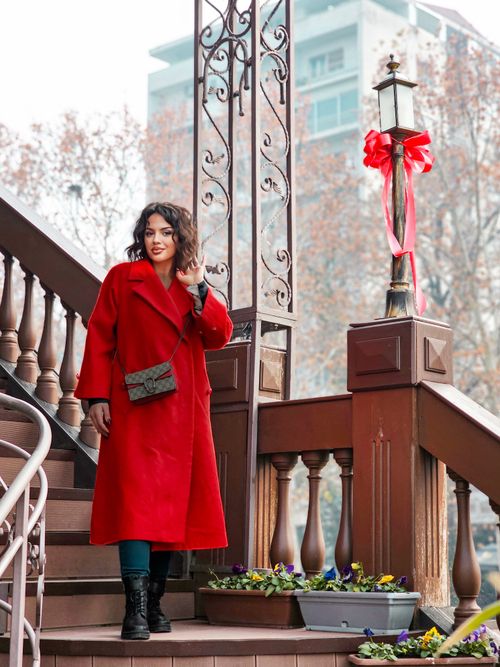 Free Elegant woman in red coat standing on a decorated staircase, sunny day. Stock Photo