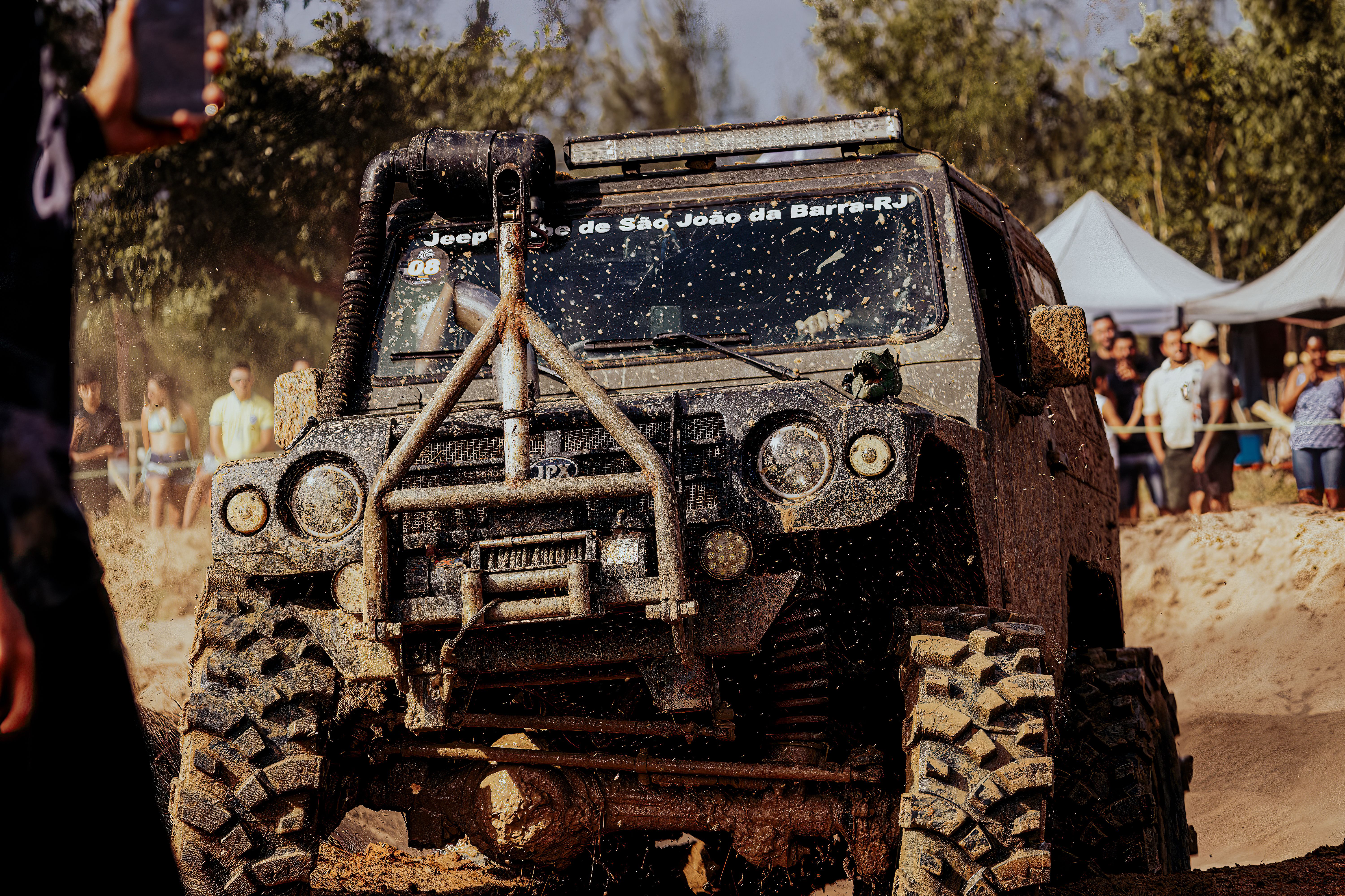 gratis Jeep rijdt over modderig terrein tijdens een offroad-evenement, terwijl toeschouwers op de achtergrond toekijken. Stockfoto