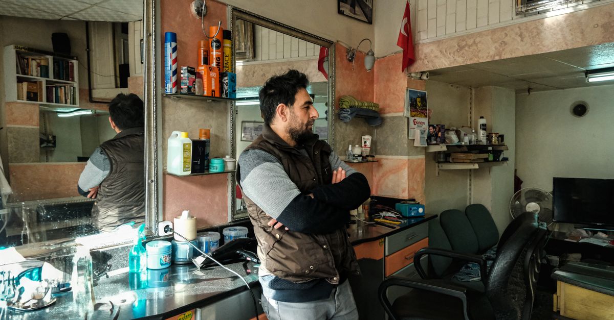 A man standing in a retro-style barbershop, reflecting in the mirror.