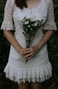 一位身着蕾丝连衣裙的女子手持白花，营造出质朴而宁静的氛围