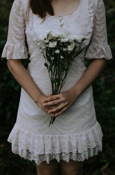 一位身着蕾丝连衣裙的女子手持白花，营造出质朴而宁静的氛围