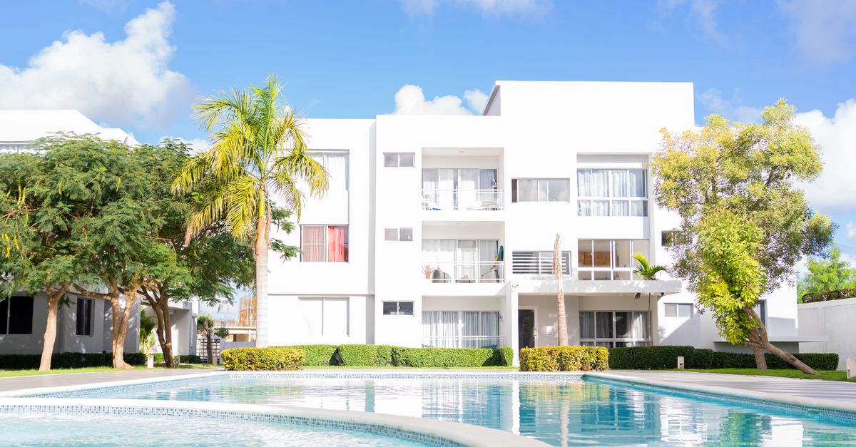Beautiful view of a modern white apartment building with a surrounding outdoor pool under a clear blue sky.