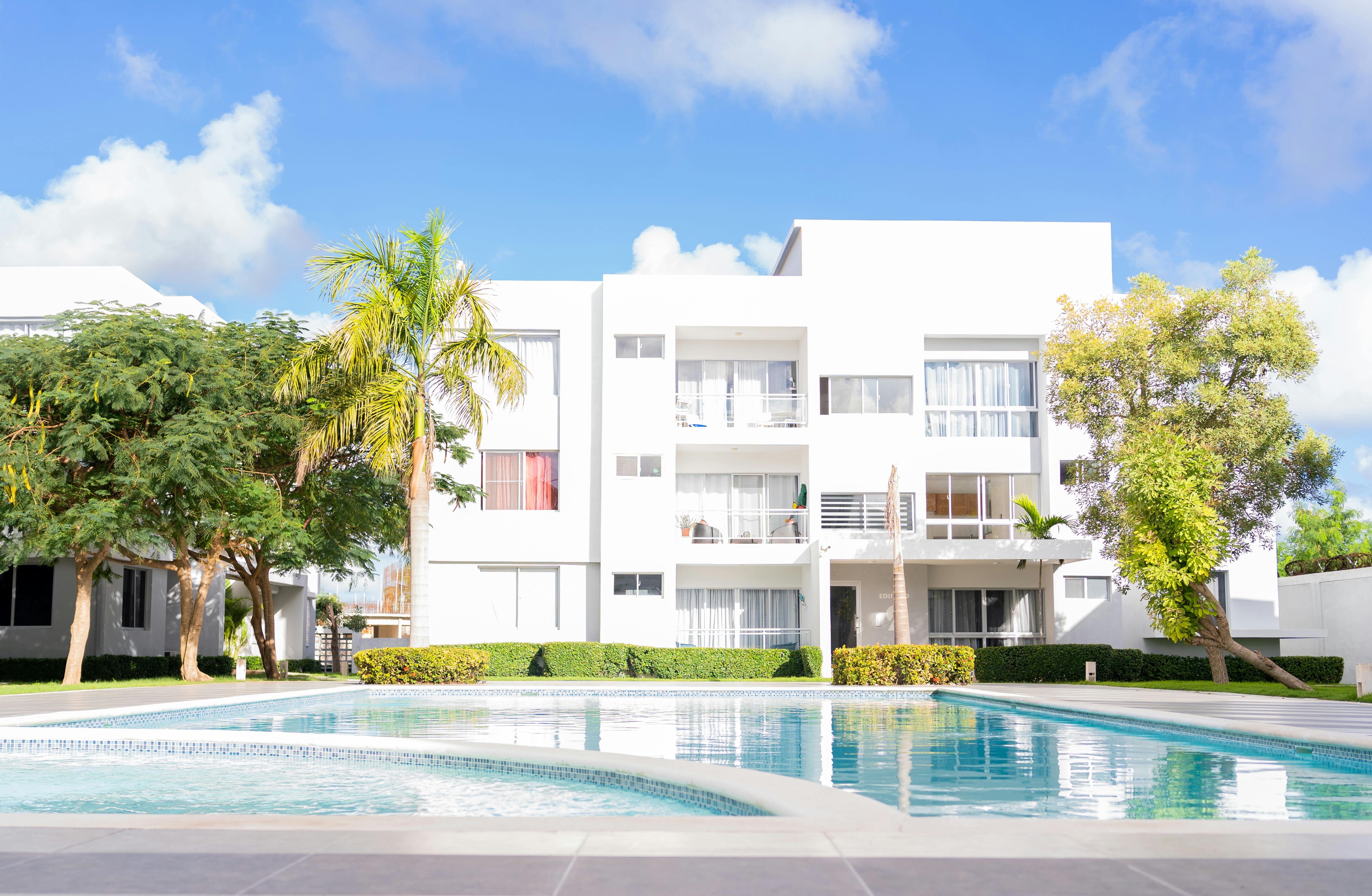 Free Beautiful view of a modern white apartment building with a surrounding outdoor pool under a clear blue sky. Stock Photo