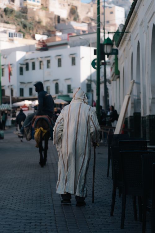 Free Elderly woman in traditional attire walking down a Moroccan street with donkey rider. Stock Photo