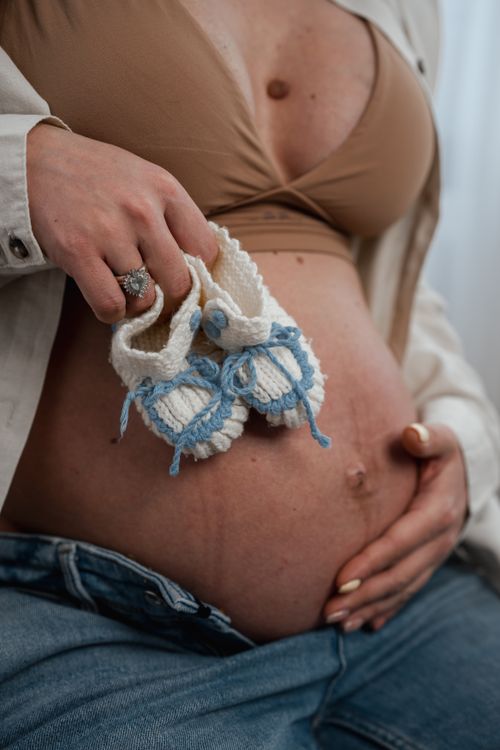 Free An expectant mother lovingly holds baby booties against her belly, symbolizing anticipation and joy. Stock Photo