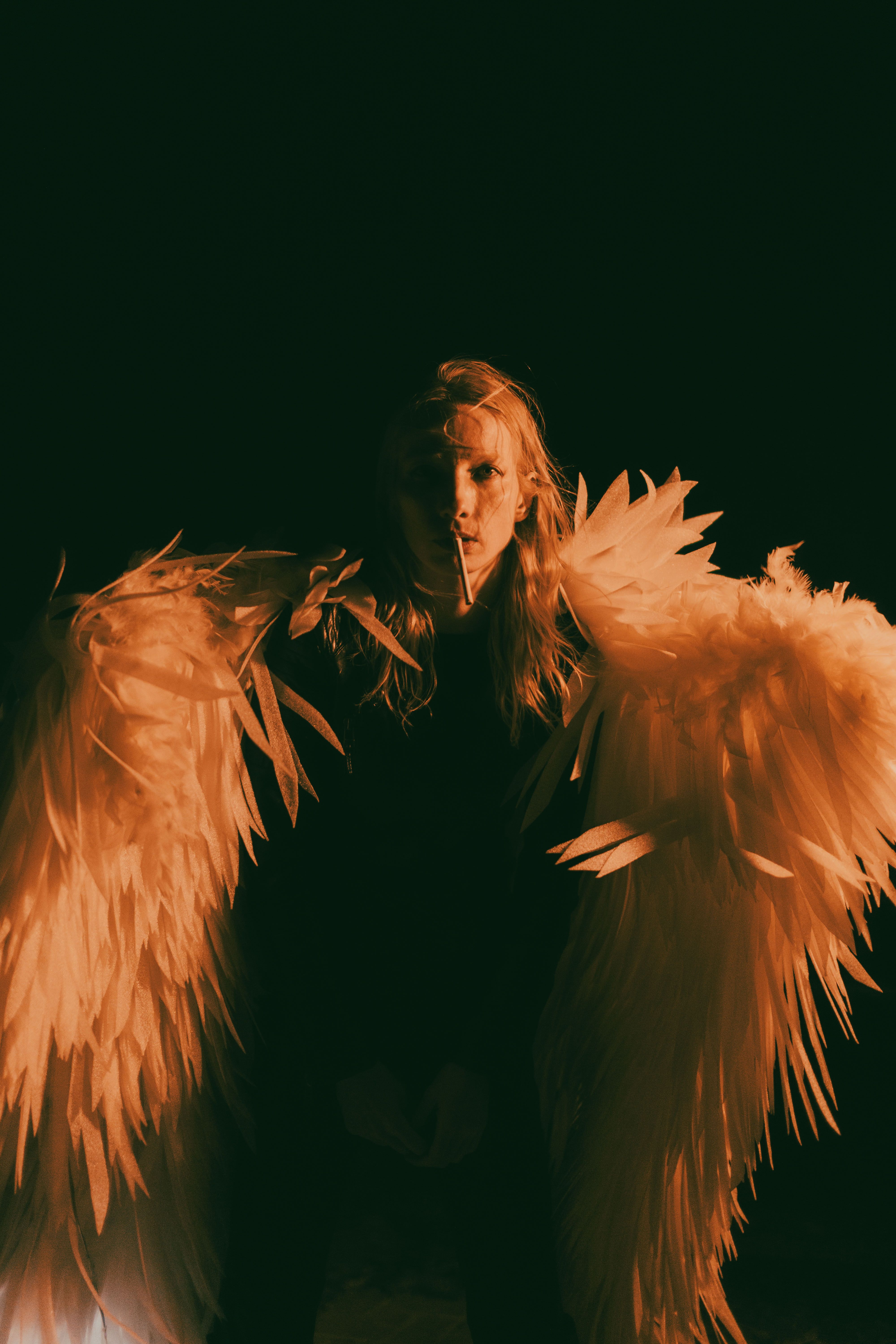 Dramatic portrait of an individual wearing angel wings in warm lighting, creating a mystical atmosphere.