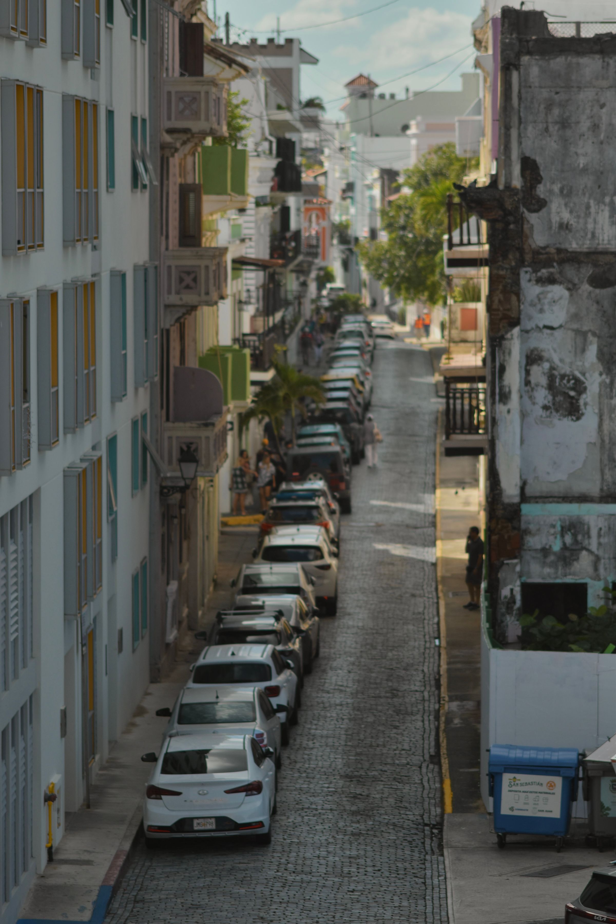 Empty blue cobblestone street, Old San Juan. Street lights still on, one open wooden window, someone sweeping — no tourists.