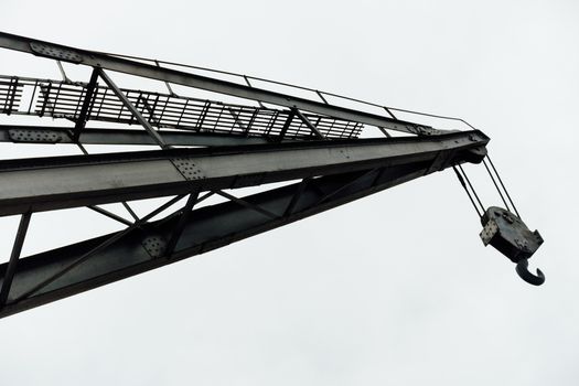 Silhouette of a steel crane arm with hook on a cloudy day, capture showing industrial strength.