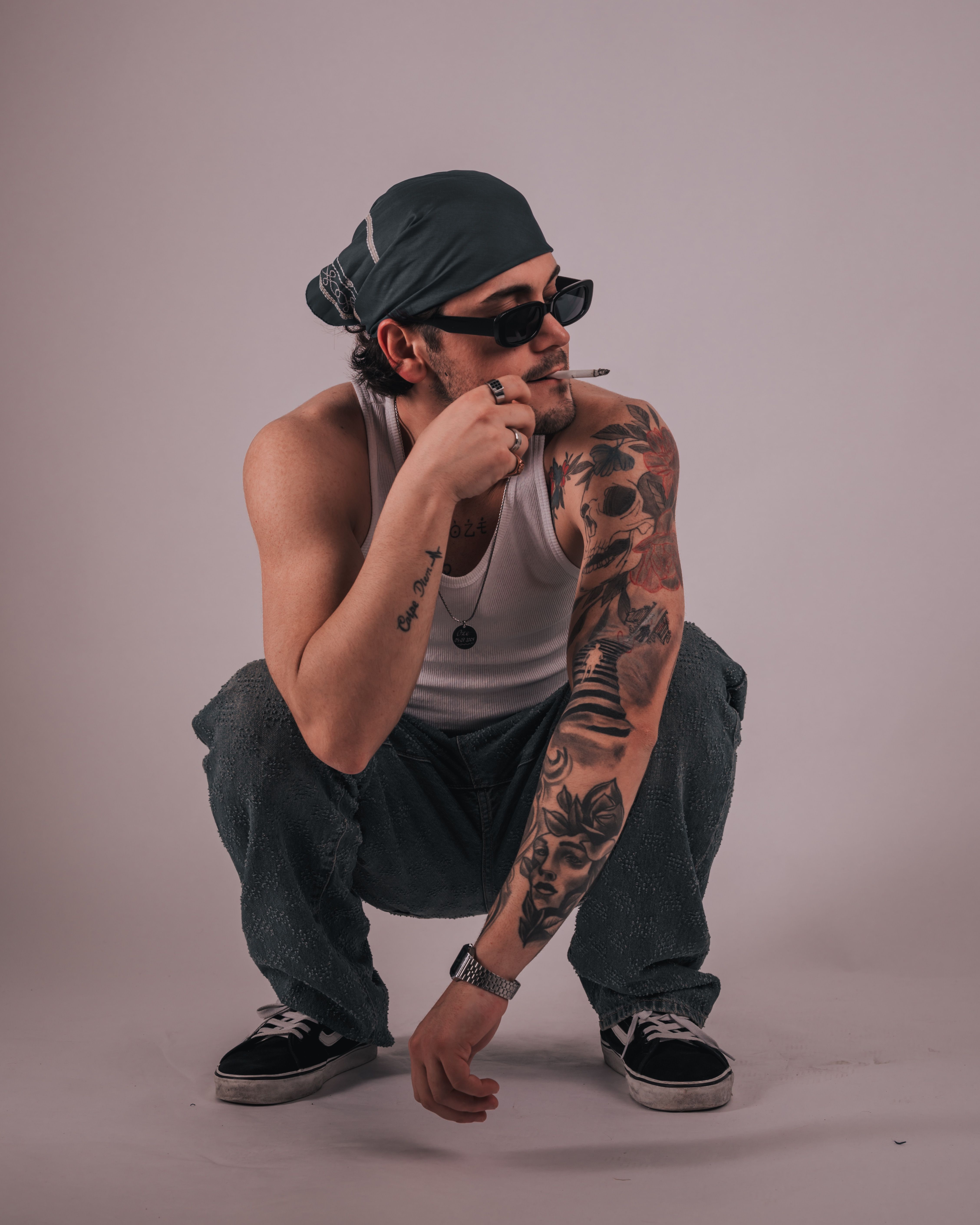 Tattooed man squatting in fashionable attire, showcasing style and attitude.
