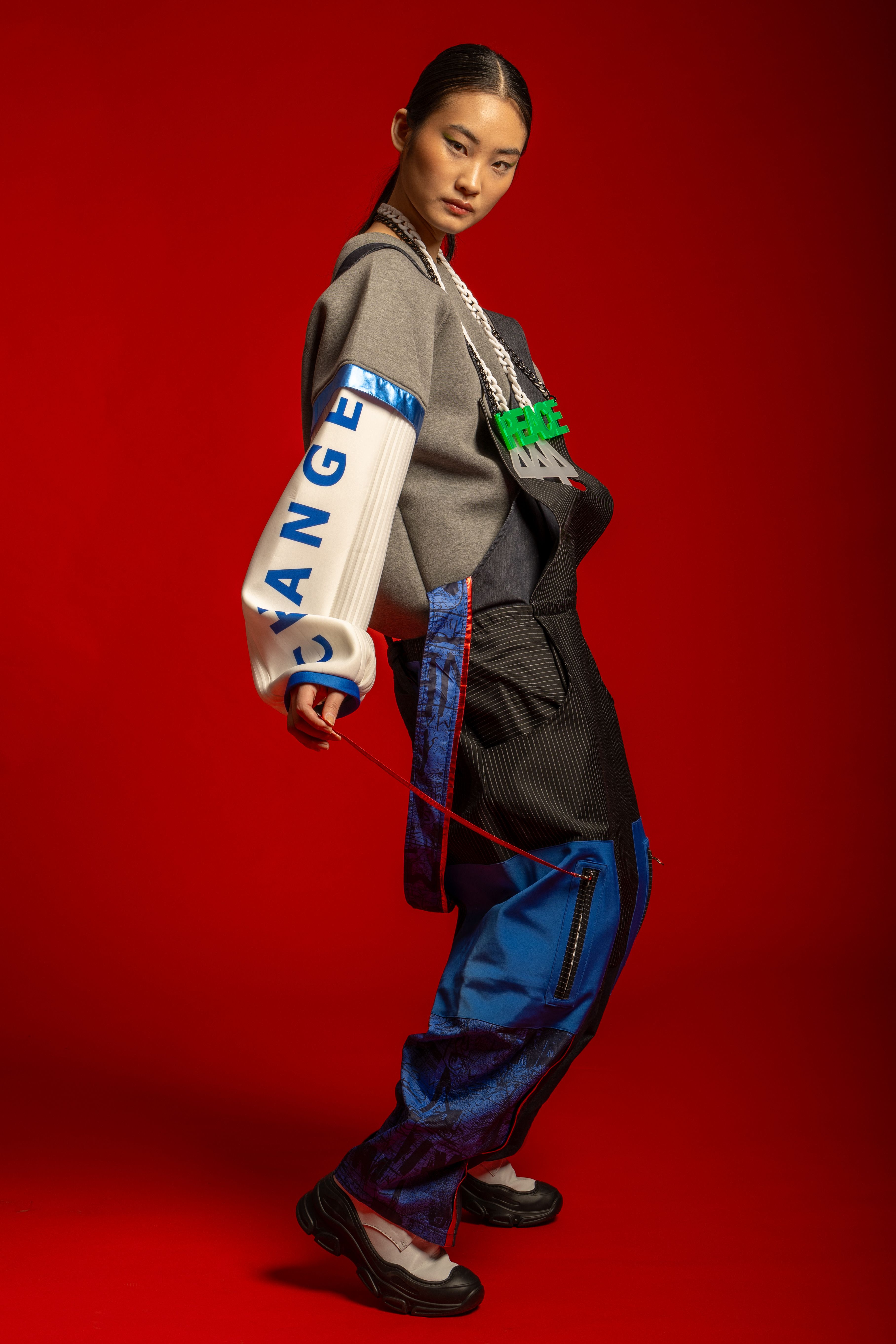 Model in avant-garde outfit against vivid red backdrop.