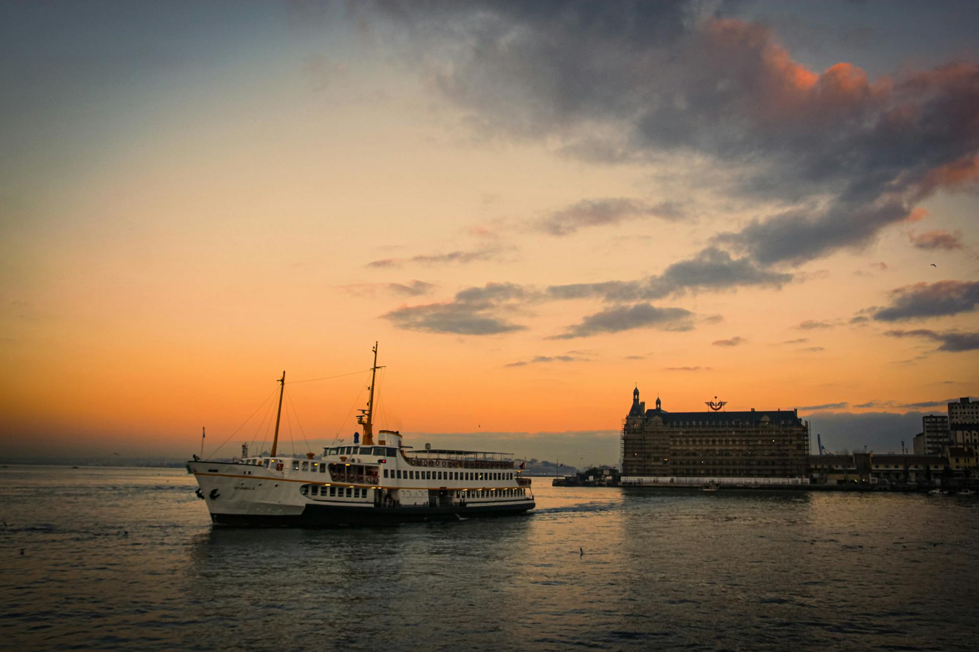 A ferry sails past a historic building at sunset, capturing the serene waters and vibrant sky.