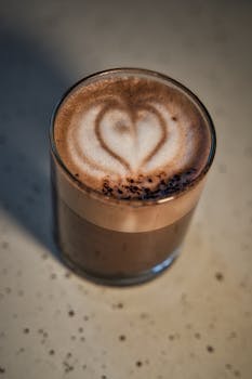 A close-up of a glass of coffee with a heart pattern in the foam, creating a warm and inviting atmosphere.