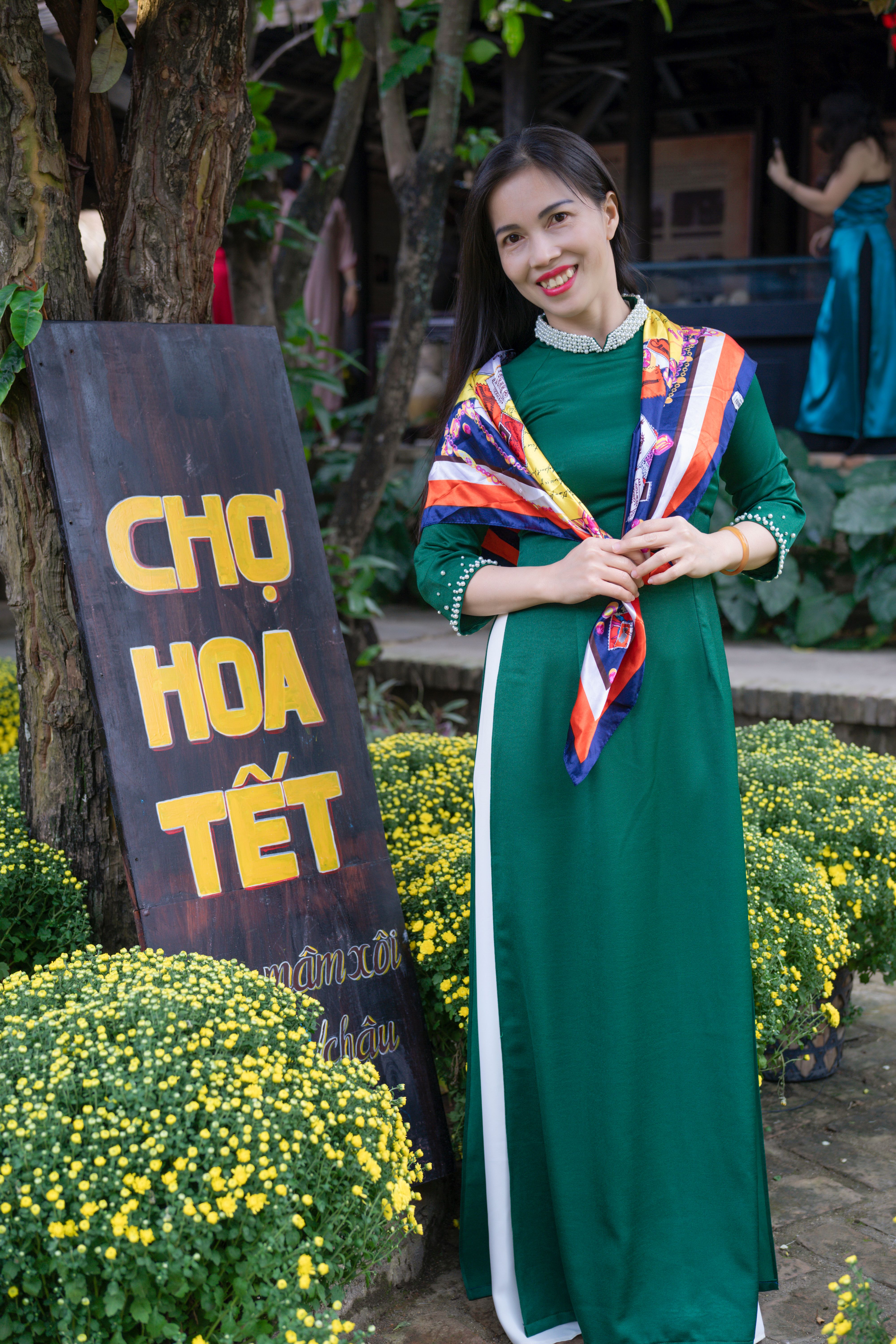 Woman in green dress enjoying Tet flower market with yellow blossoms.