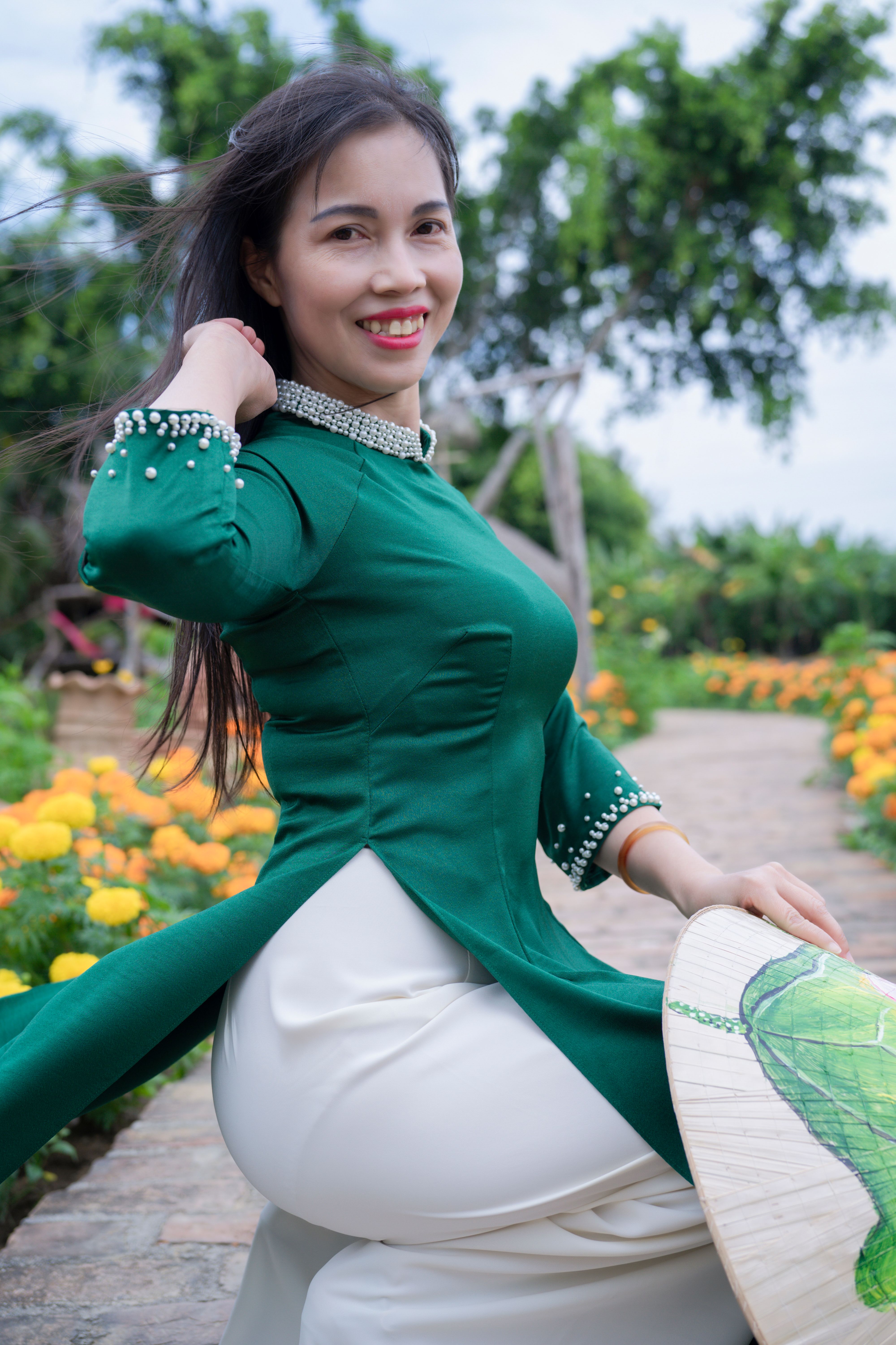 Smiling woman in traditional green ao dai outdoors in a vibrant flower garden.