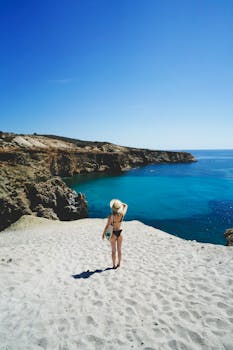 夏日阳光明媚，一位身着泳衣的女子从沙质悬崖上欣赏着海岸景色