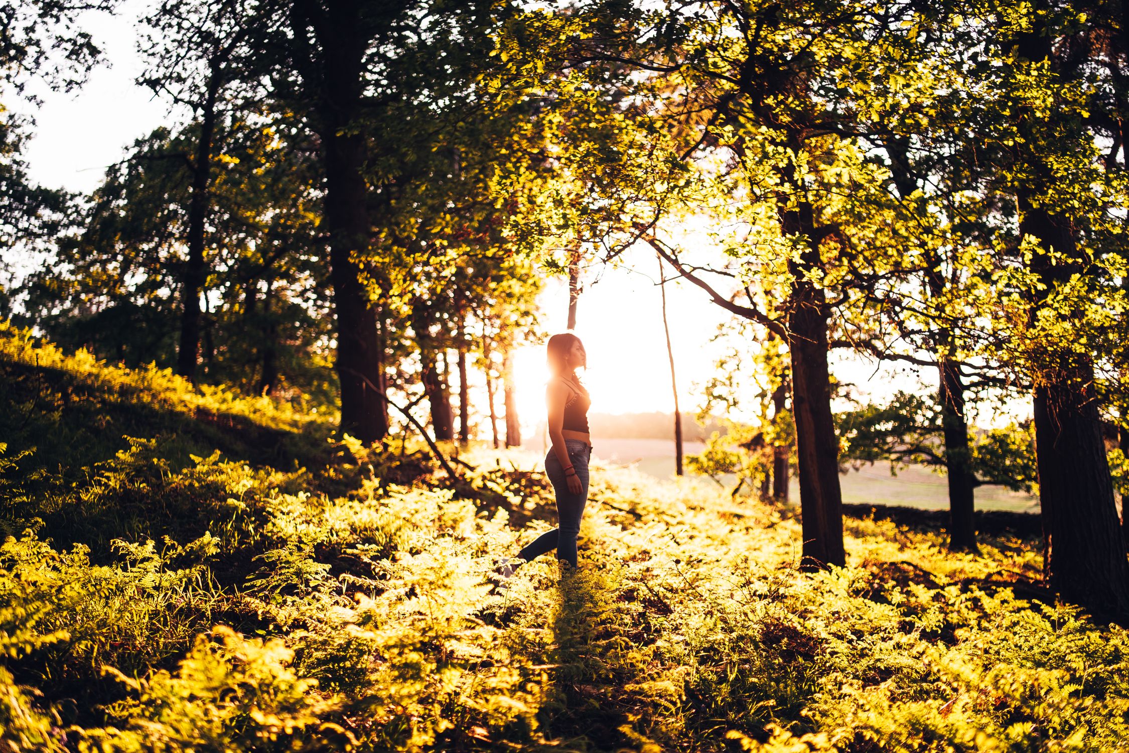 Woman walking through a sunlit forest during golden hour, peaceful and free