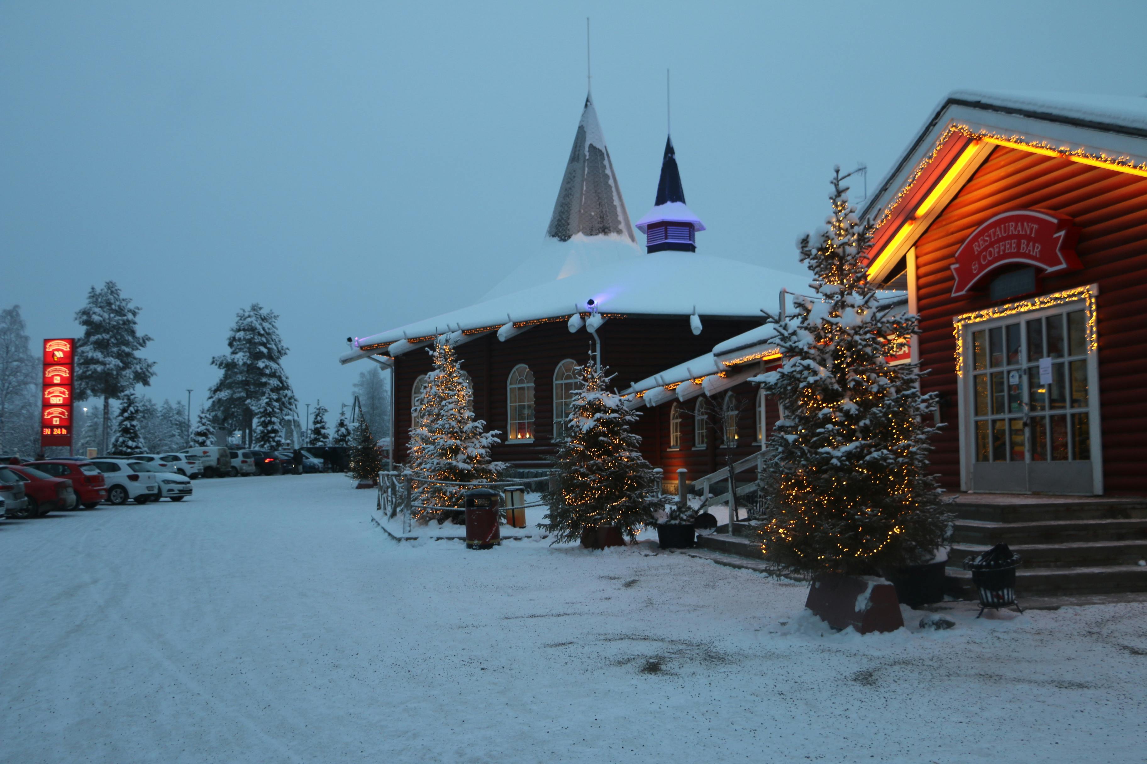 Snowy scene of wooden buildings decorated with Christmas lights in Rovaniemi, Finland.