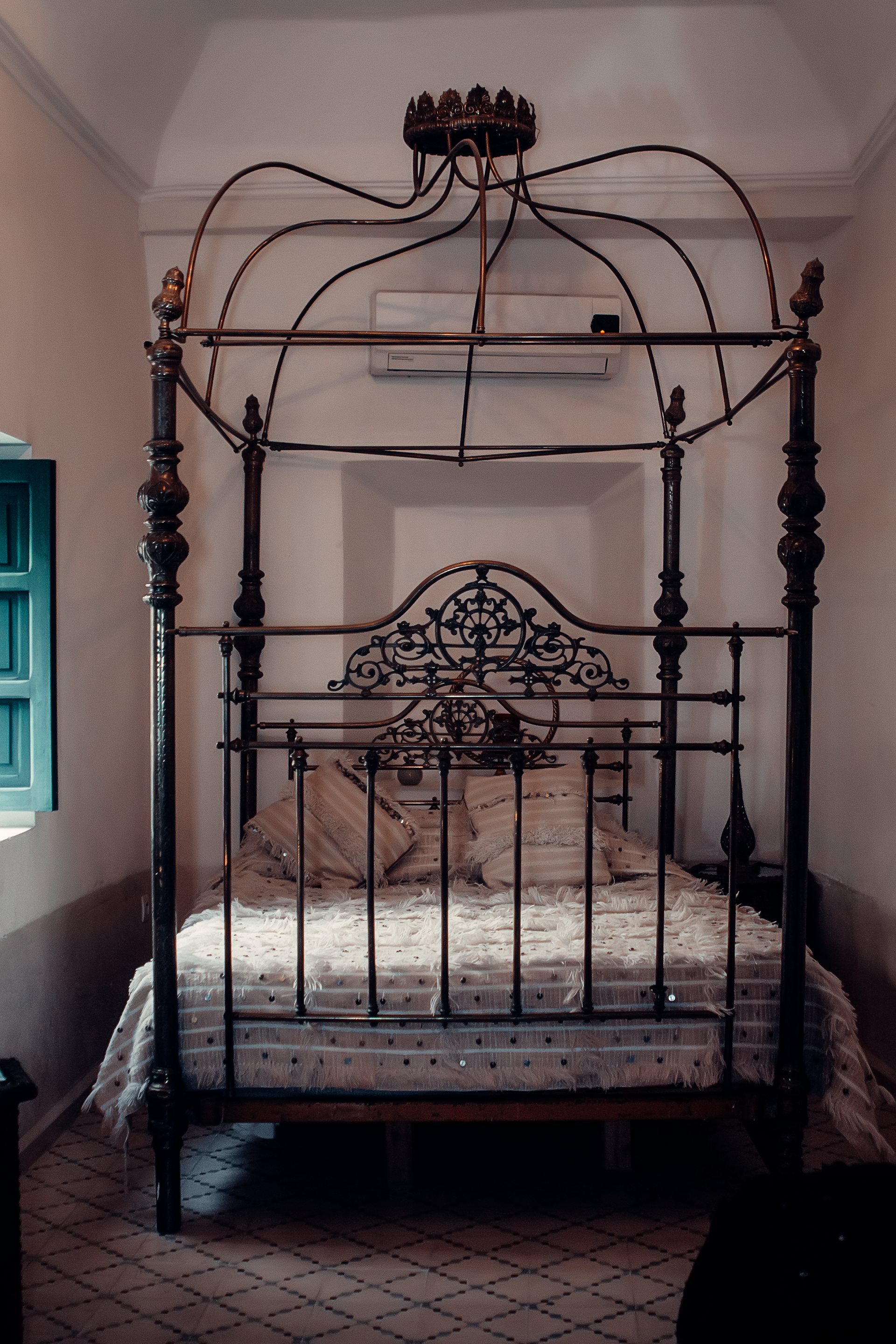 Ornate wrought iron bed in a Moroccan riad with traditional decor and bedding.