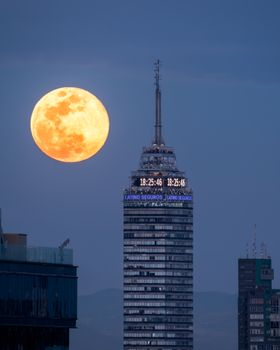 The full moon rises over the iconic Torre Latinoamericana in Mexico City at night.