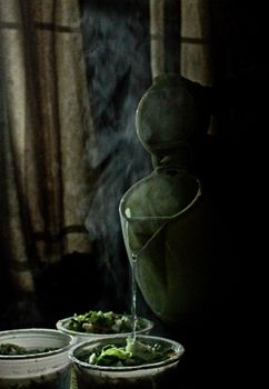 Moody shot of hot tea being poured into cups, creating steam in a dimly lit room.