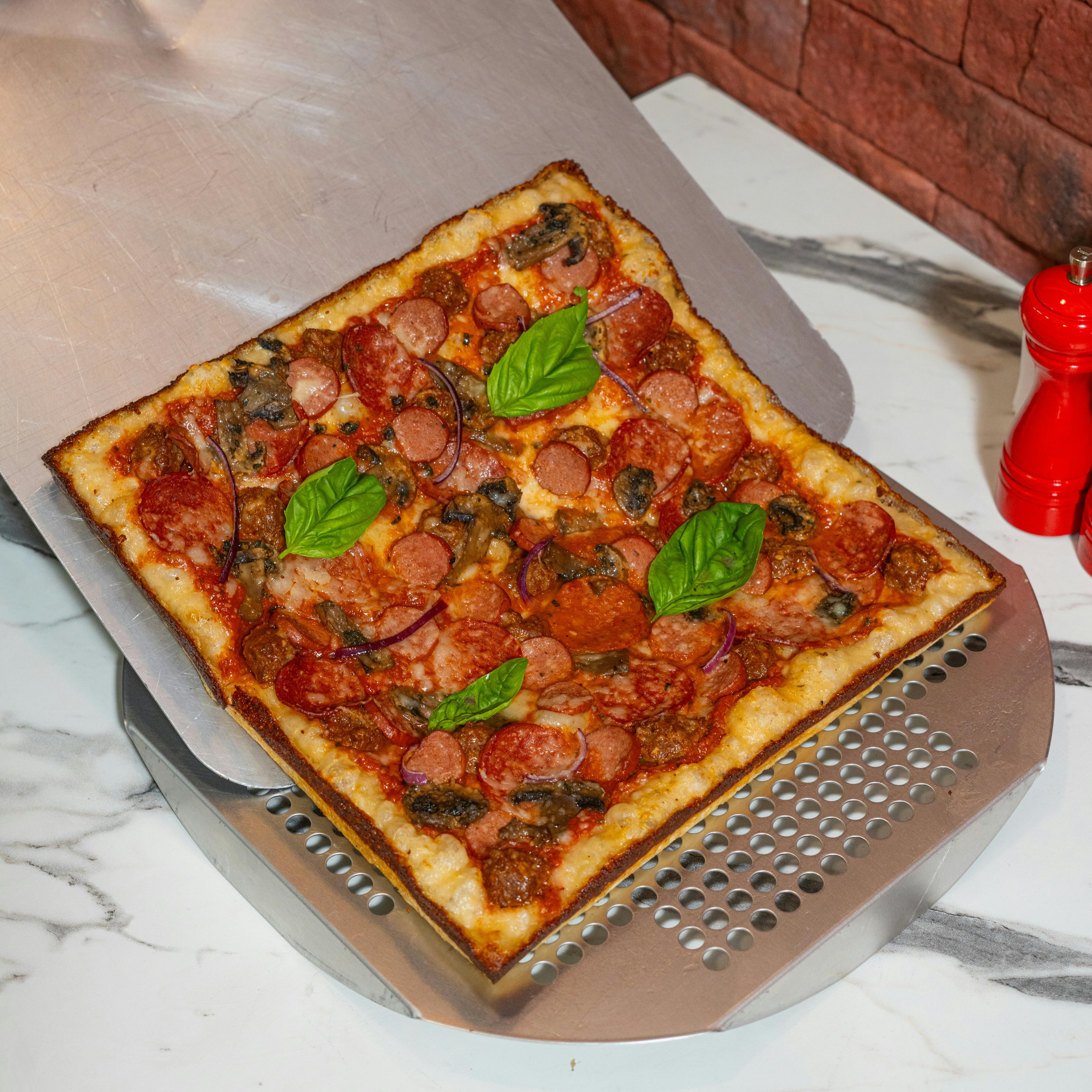 Delicious square pepperoni pizza with fresh basil leaves, served on a pizza peel in a modern kitchen.