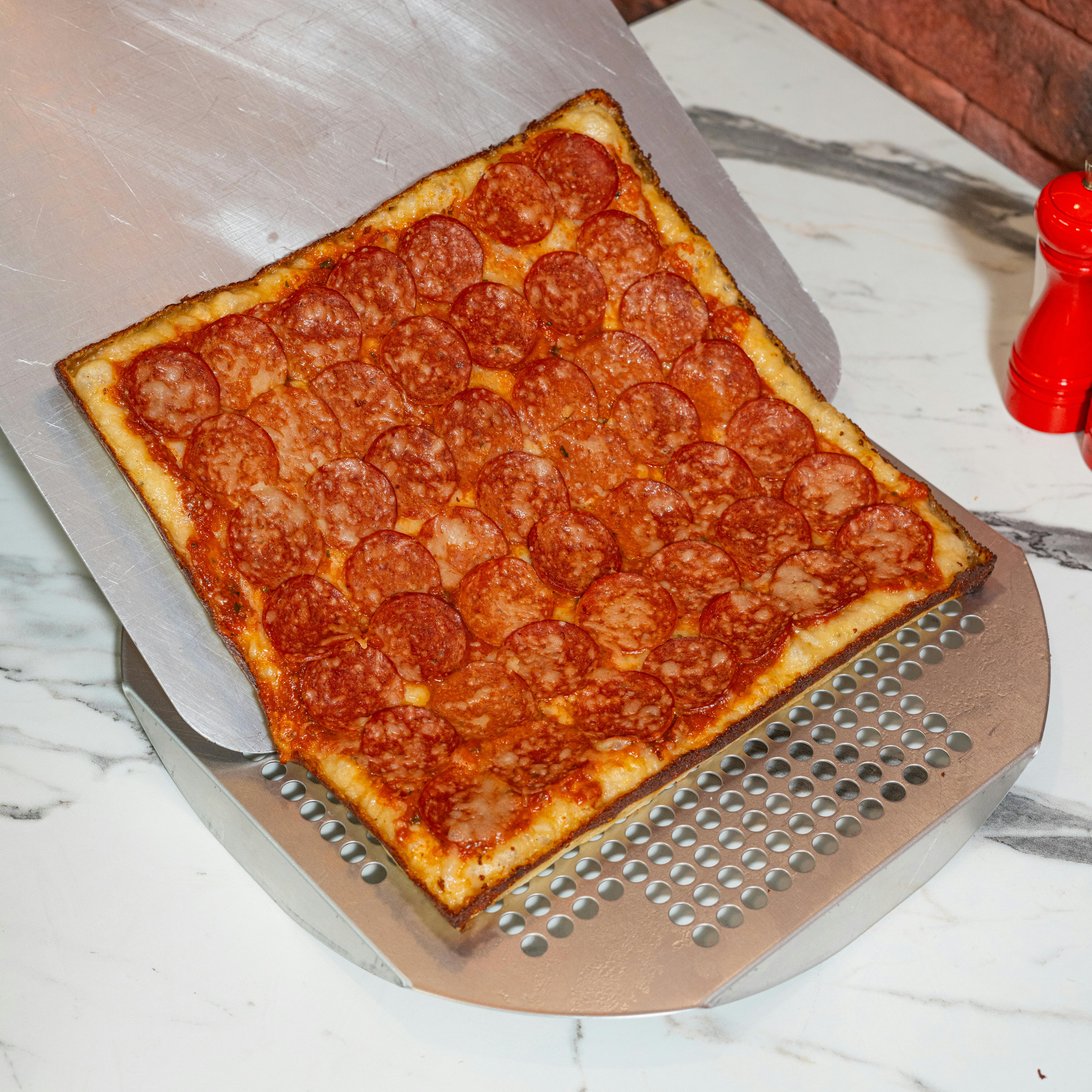 Freshly baked square pepperoni pizza on a marble surface with a pizza peel.