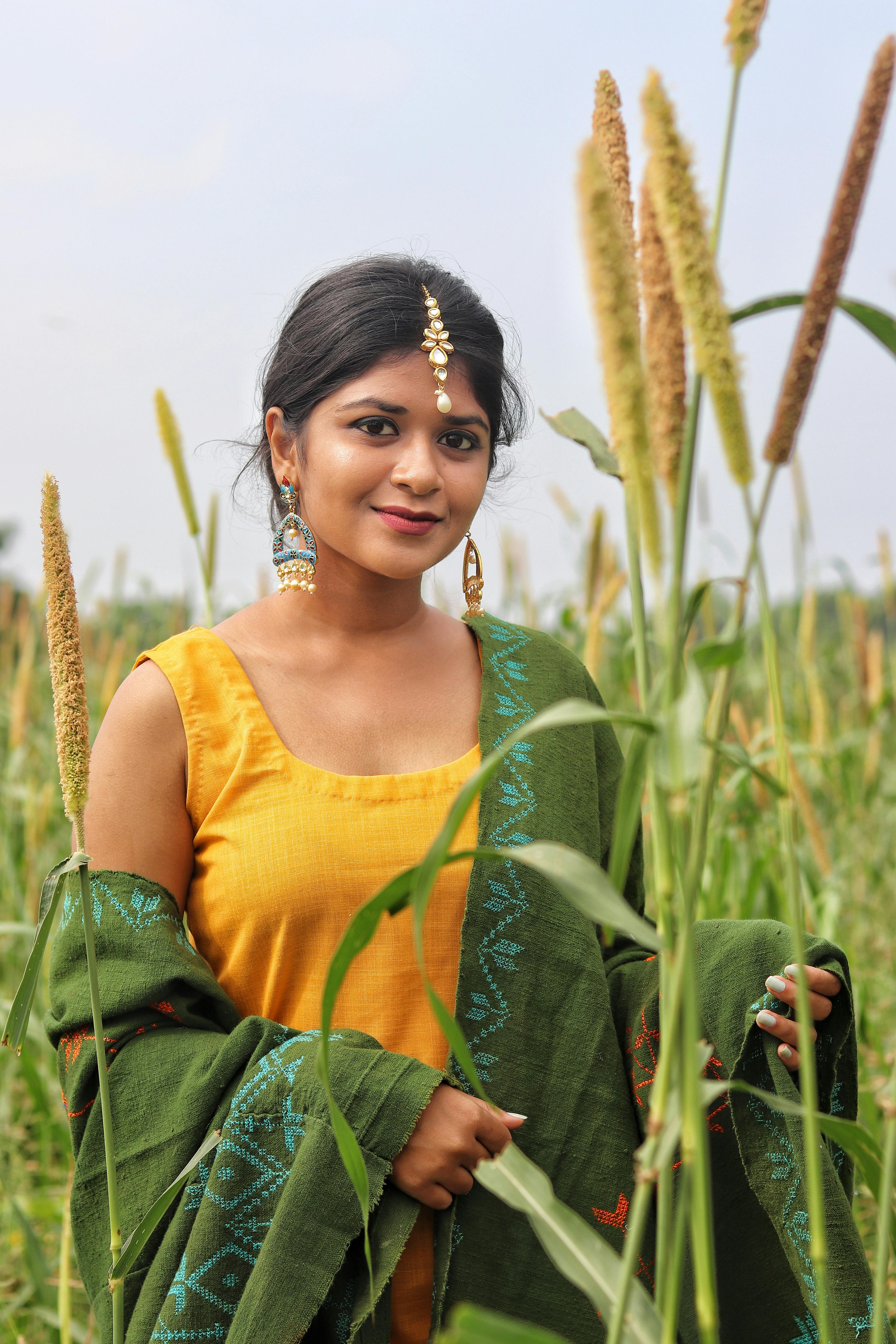 A young woman wearing traditional clothing smiles in a green field during summer.