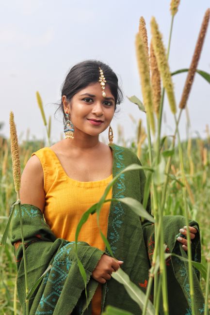 A young woman wearing traditional clothing smiles in a green field during summer.