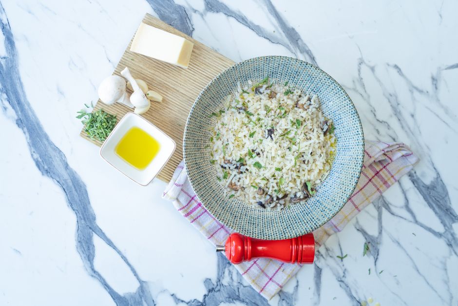 Top view of a flavorful mushroom risotto with cheese, olive oil, and herbs on a marble counter.