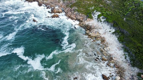 Free Stunning aerial view of a rocky coastline with vibrant green foliage and turquoise sea waves. Stock Photo