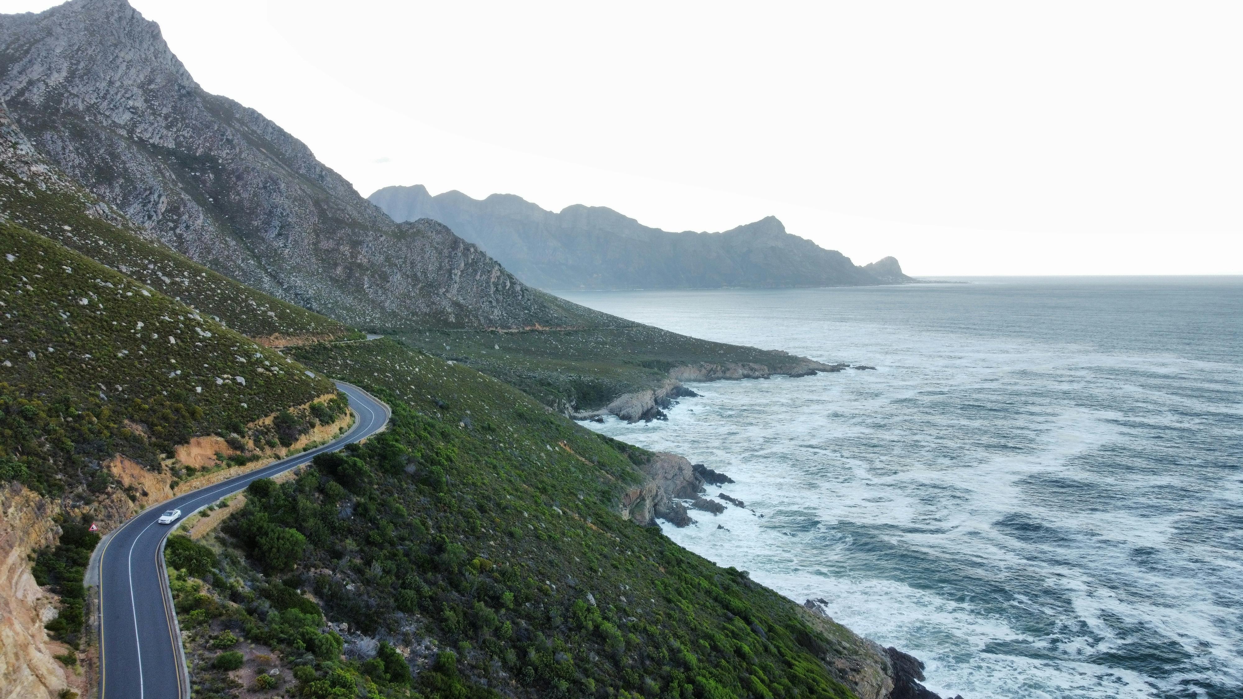 A breathtaking coastal road curves through a mountainous landscape along the ocean.