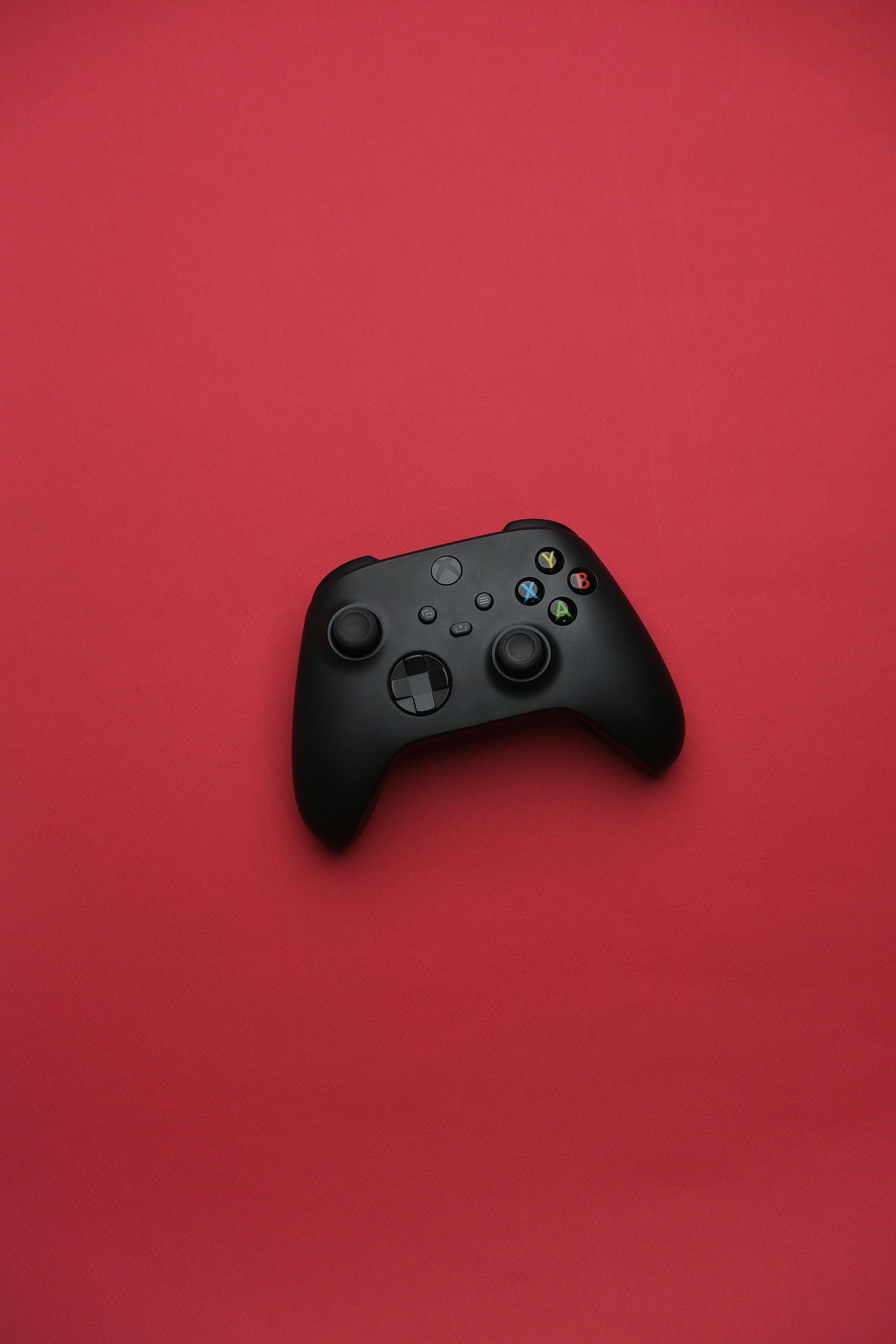 Minimalist photo of a black gaming controller on a vivid red background.