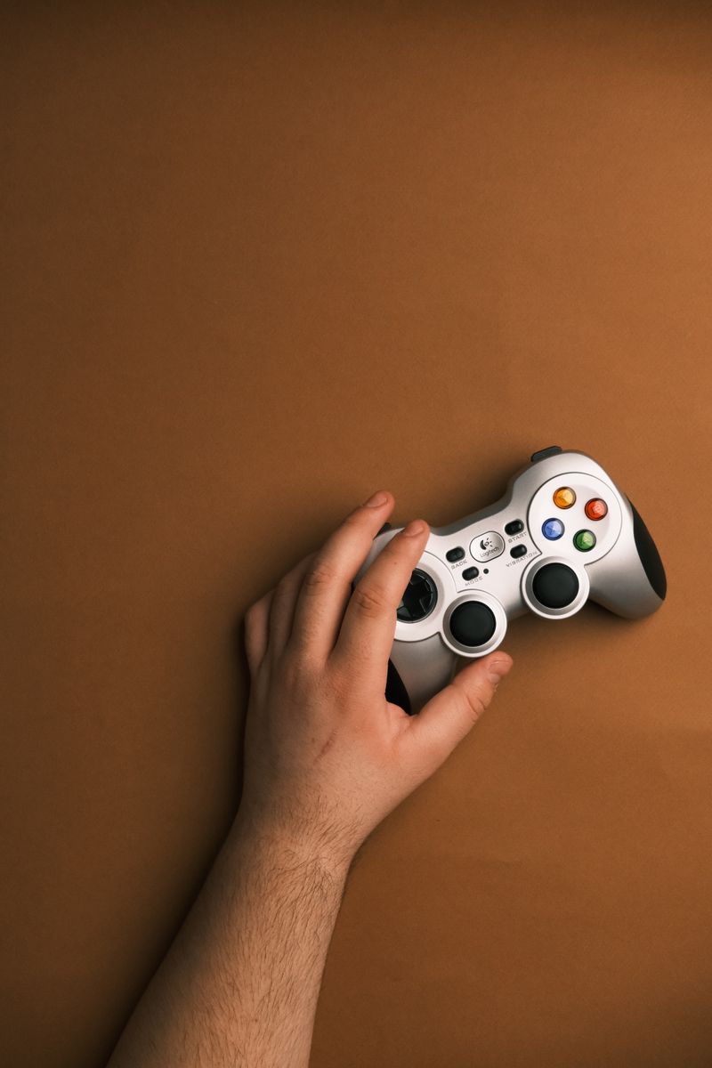 A hand holding a white game controller on a brown background, showcasing gaming culture.