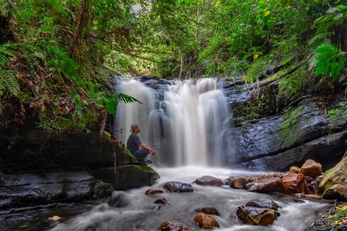 Free Man sitting by a waterfall in a lush green forest in Amazonas, Peru. Stock Photo