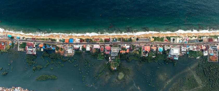 Panoramic aerial shot of a coastal village with ocean and lush greenery.