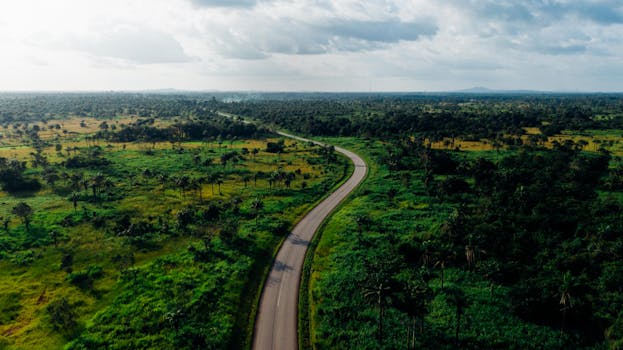 Aerial view of a winding road cutting through lush green countryside under a cloudy sky.