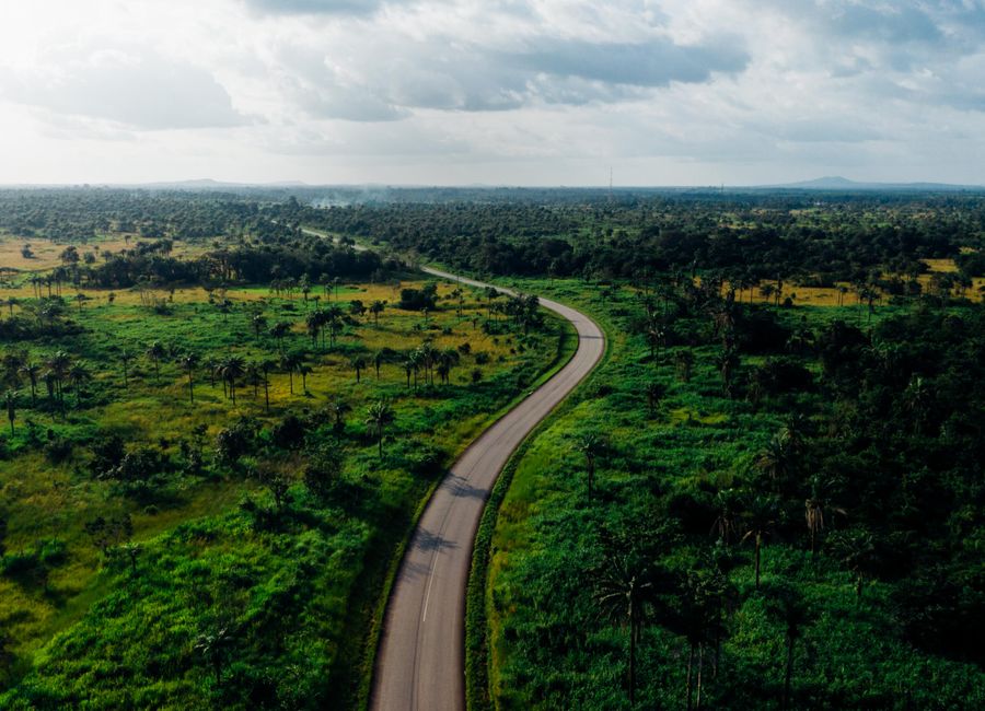 Aerial view of a winding road cutting through lush green countryside under a cloudy sky.