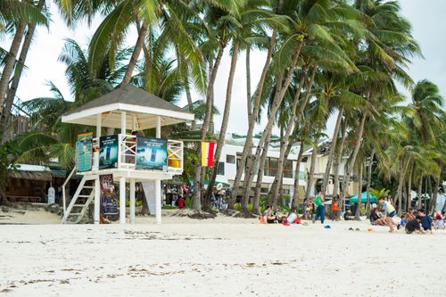 Free Lively tropical beach scene with palm trees, people relaxing, and a lifeguard tower. Stock Photo