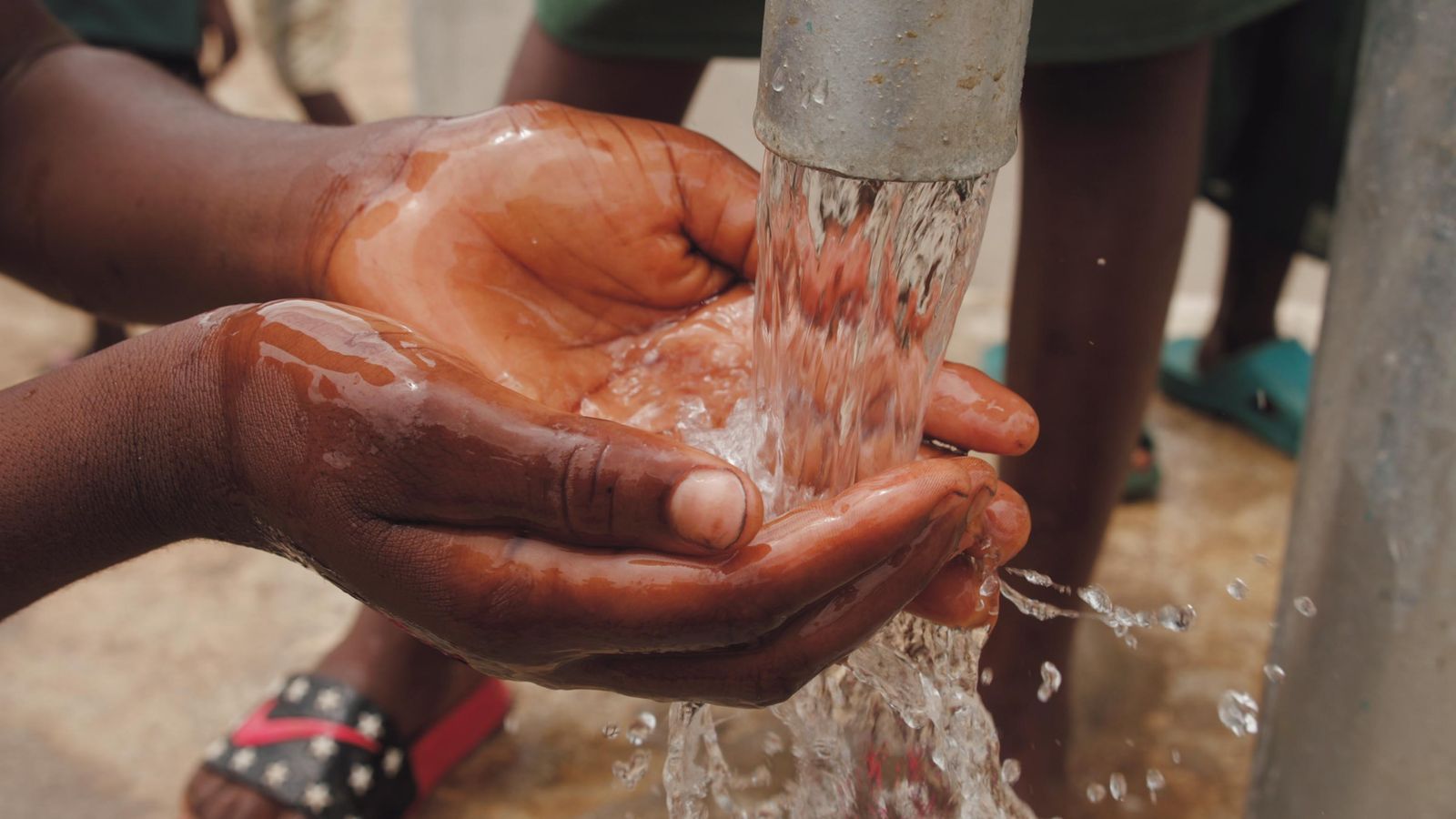 Hands capturing fresh water from a pump