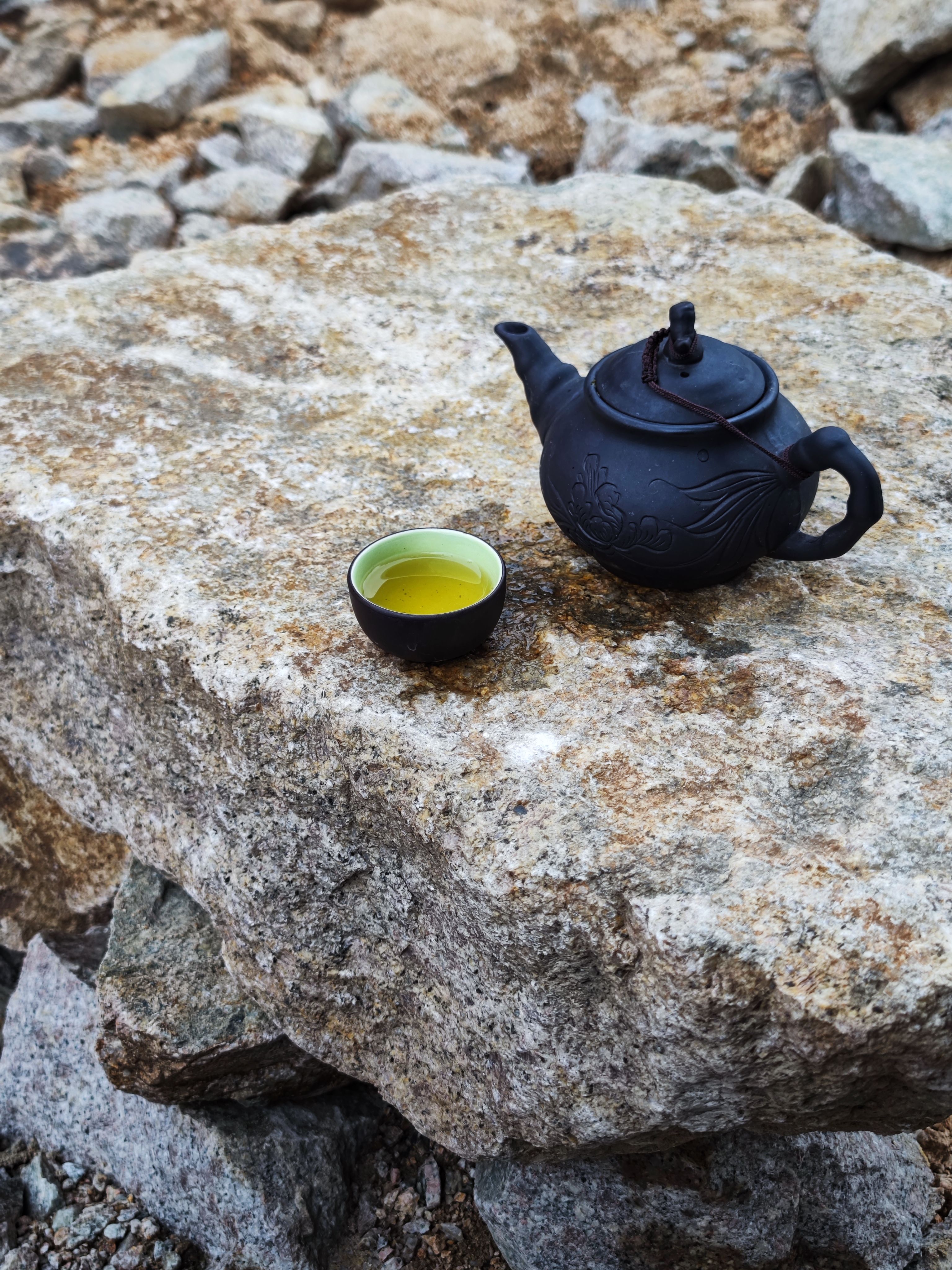 A traditional black teapot and cup with tea placed on a natural stone surface outdoors in Vietnam.