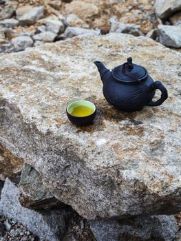 A traditional black teapot and cup with tea placed on a natural stone surface outdoors in Vietnam.